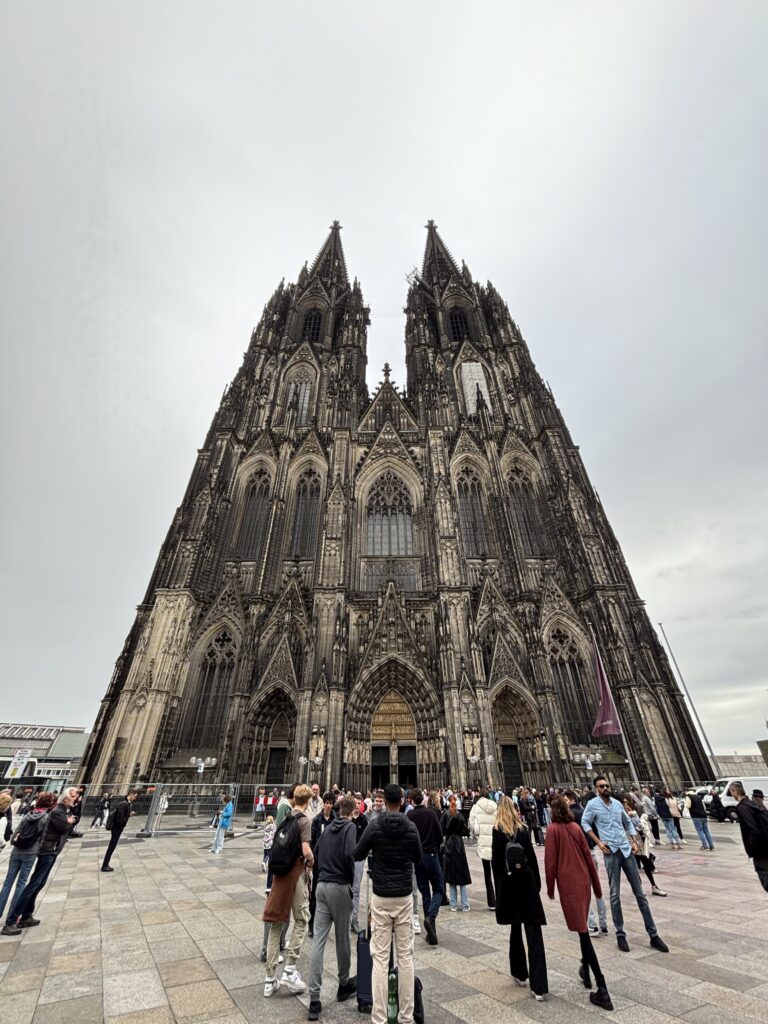 An intricated facade raises up to the sky, a lot of people are in the ground in front of the building