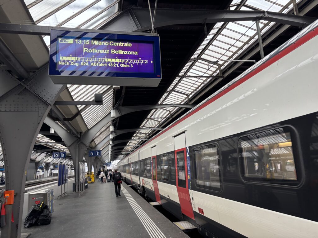 A white and red train at a platform. A destination sign shows the destination of the train.