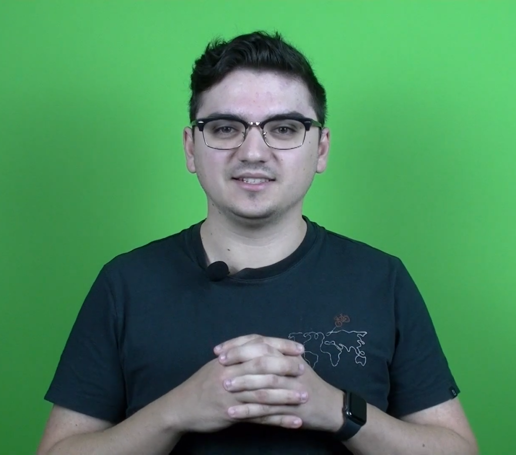 A man talking while holding hands, with a green screen on the back