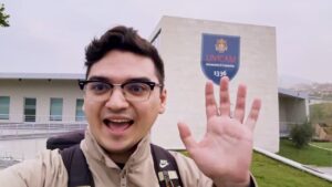 A man waving in a happy mood, with a building on the background